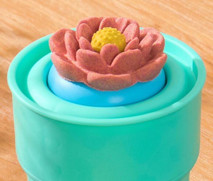 Easter treasure: decorative flower candle in a teal holder on a wooden surface.
