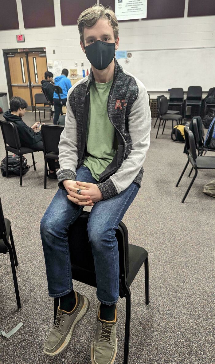 Person sitting on two chairs looking like one, creating an illusion.
