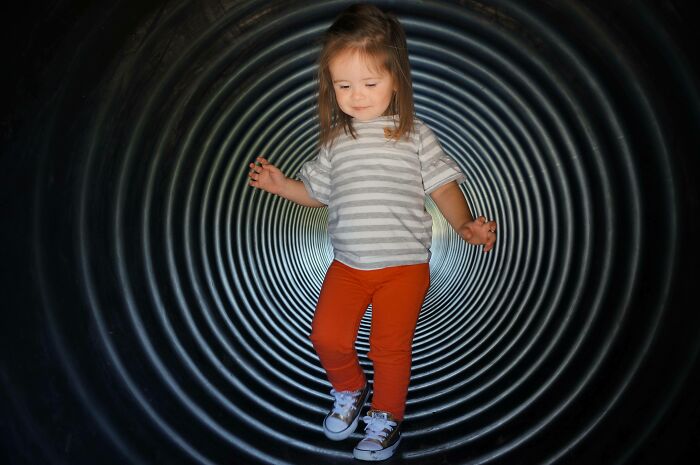 Child in playful stance inside an optical illusion spiral tunnel, appearing surreal but is real.