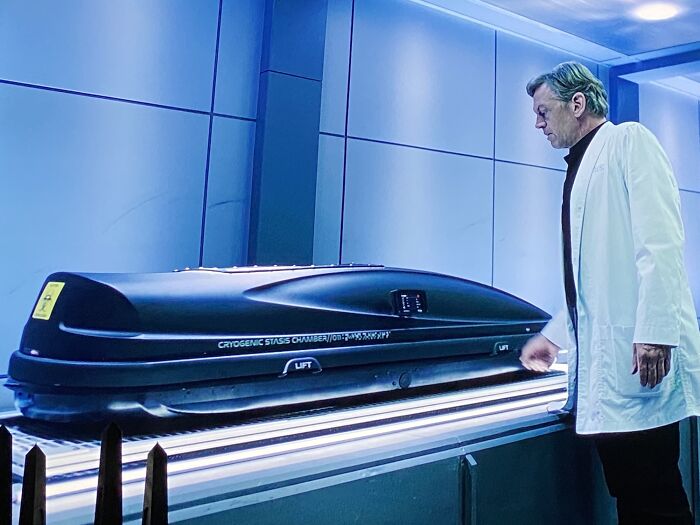 A filmmaker inspects a futuristic cryogenic stasis chamber prop.