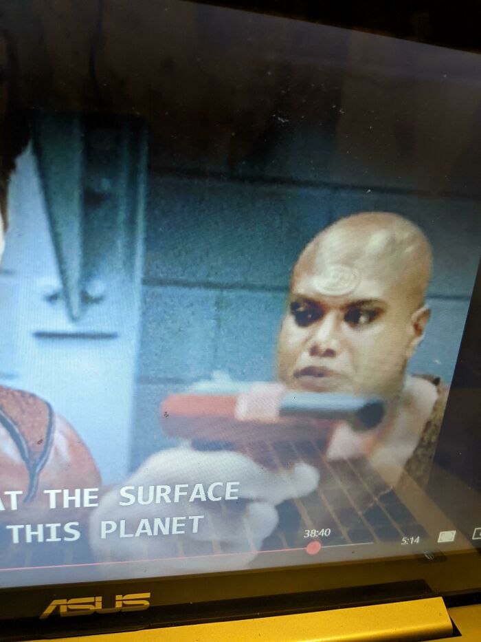 Bald character holding a prop gun creatively designed, displayed on a laptop screen during a movie scene.