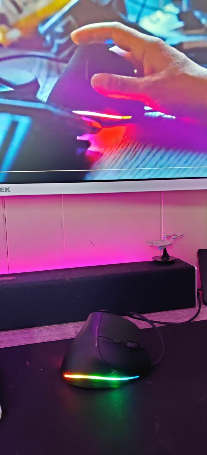 A creative approach to props with a glowing ergonomic mouse and TV reflection in a tech setup.