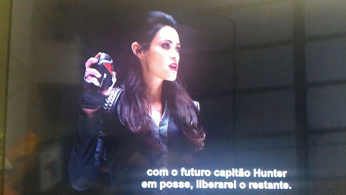 Actress holding a creative prop in a dramatic scene with Portuguese subtitles visible at the bottom.