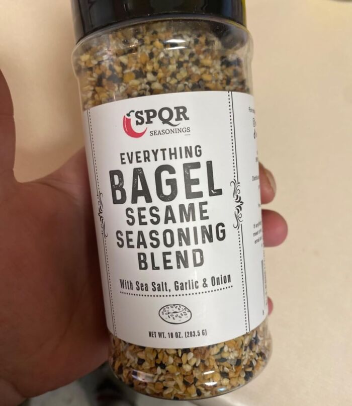 Jar of everything bagel sesame seasoning blend in hand, featuring sea salt, garlic, and onion, evoking millennial nostalgia.
