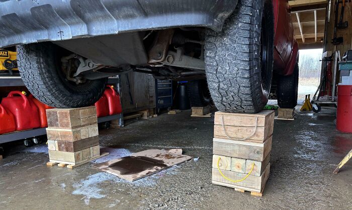 Car dangerously elevated on unstable wooden blocks in a garage setting.