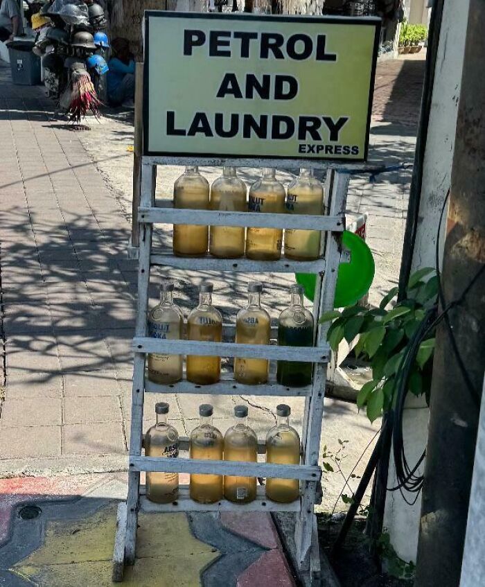 Dangerous display of petrol bottles on a sidewalk shelf near a "Petrol and Laundry" sign.