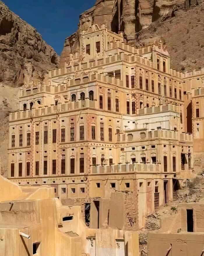 Ancient multi-story building set against a rocky cliff, showcasing historical architecture.