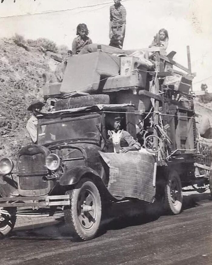 Vintage photo of a loaded car journeying on a road, with passengers atop, illustrating a moment from history enthusiasts' archives.