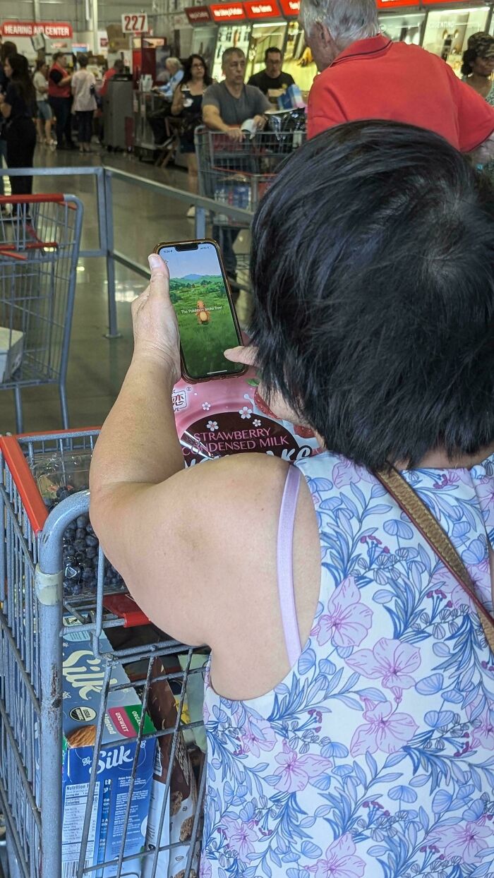 Elderly person in grocery aisle playing game on smartphone, showcasing humor and tech-savvy nature.