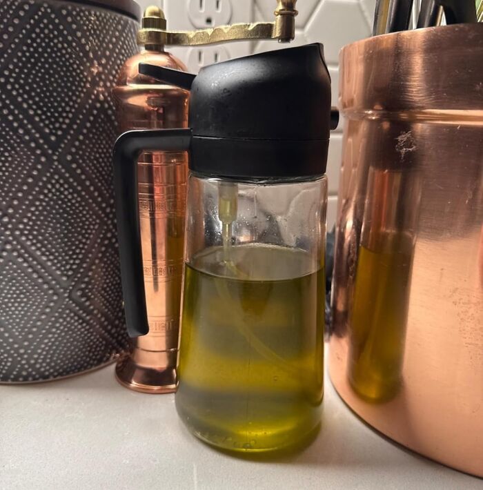 Amazon movers and shakers: Glass oil dispenser with black top on a kitchen counter near copper and patterned containers.