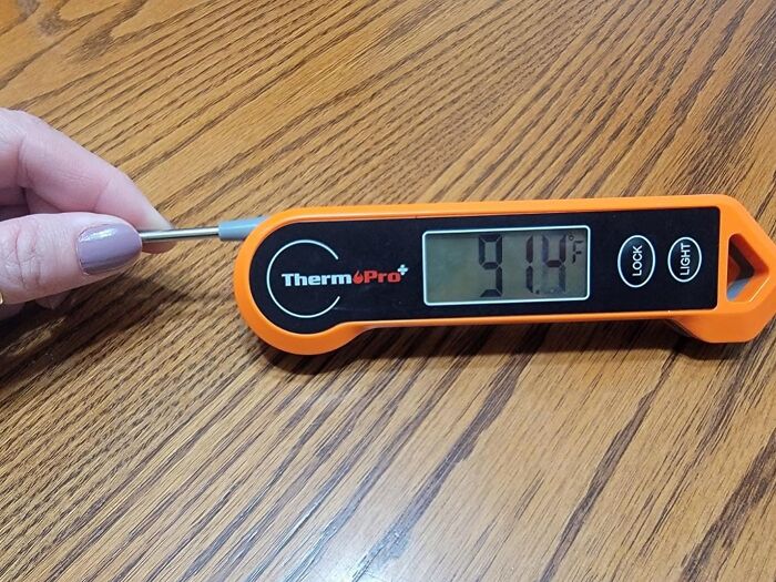 Hand holding ThermoPro digital thermometer showing 91.4°F on wooden surface, a popular Amazon mover and shaker.