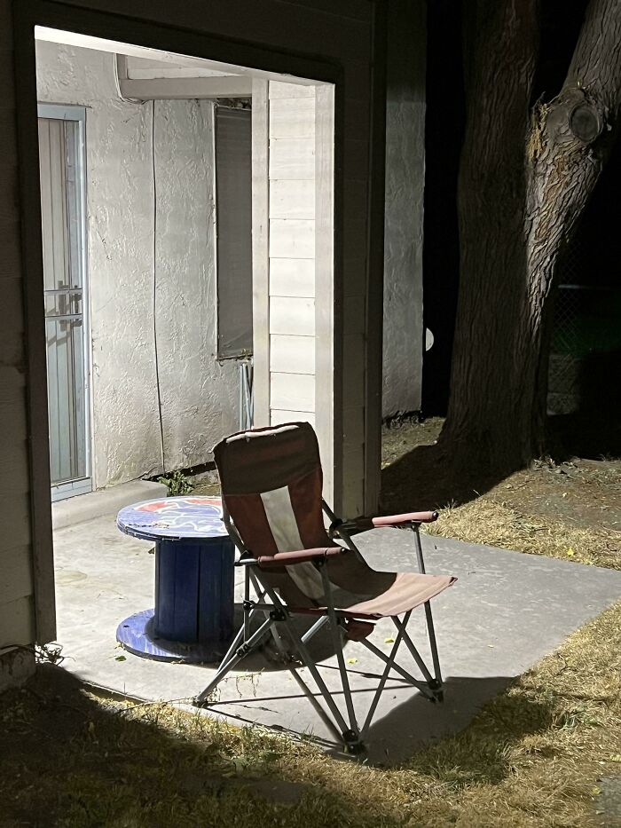 A folding chair and table on an outdoor patio at night, illustrating horrific landlord neglect.