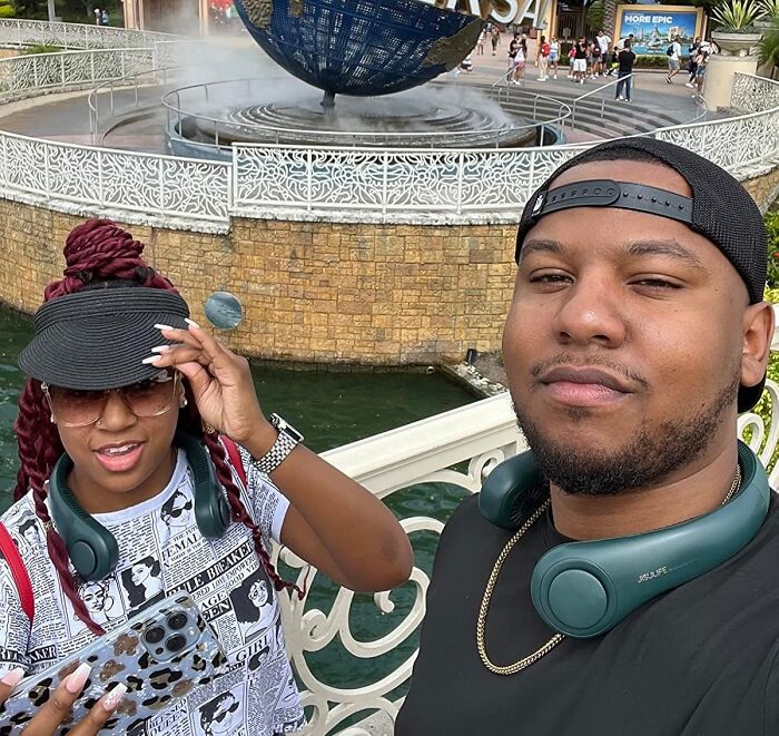 Two people wearing headphones at a theme park with a globe fountain in the background, related to 40K Review Club.