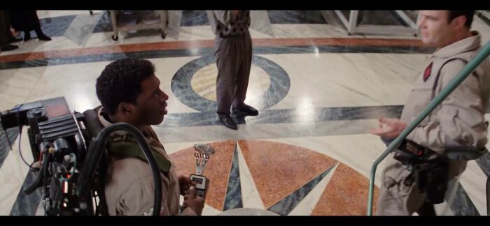 Two filmmakers in a creative scene discussing props on a patterned marble floor.