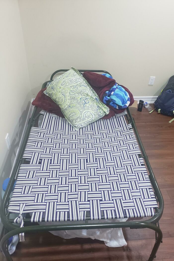 Worn cot with patterned bedding in a dim room, depicting challenges with landlords.