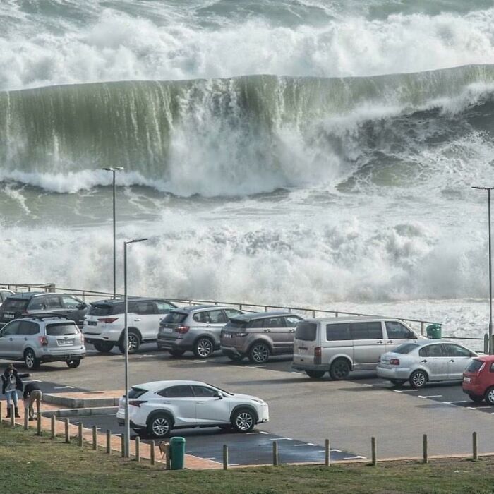 Massive ocean waves crashing near a parking lot, creating a dramatic and scary scene.