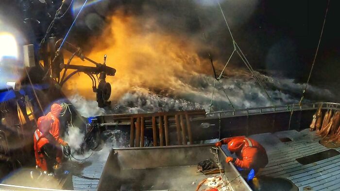 Fishermen in red gear battle rough ocean waves at night, emphasizing the ocean's daunting power.