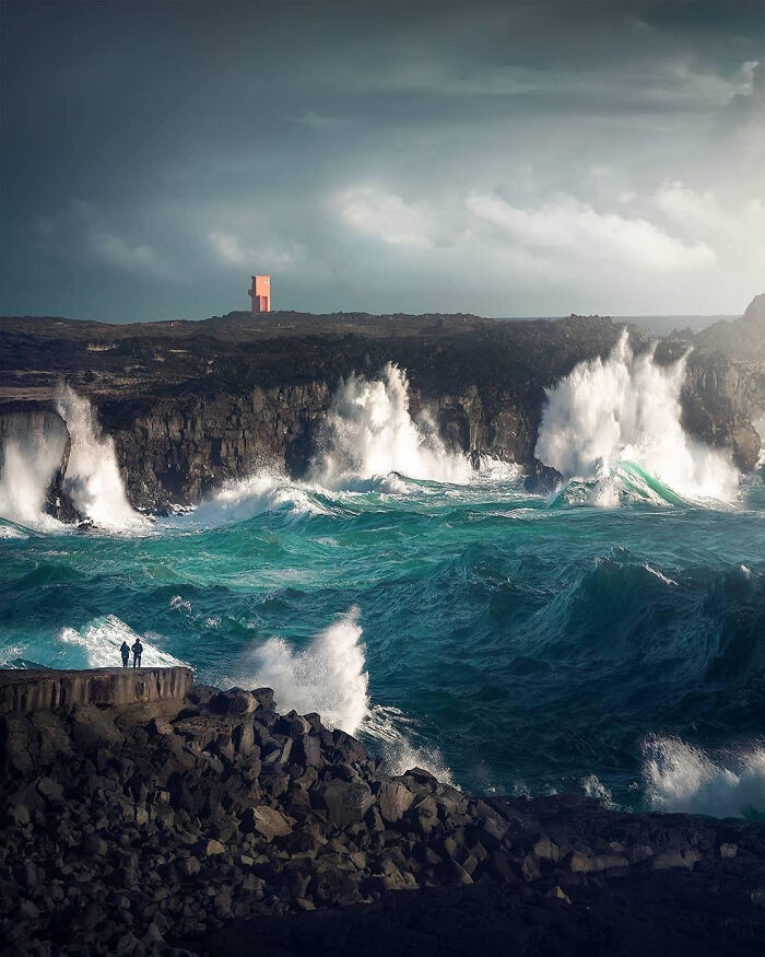 Stormy ocean waves crashing against rocky cliffs under a cloudy sky.