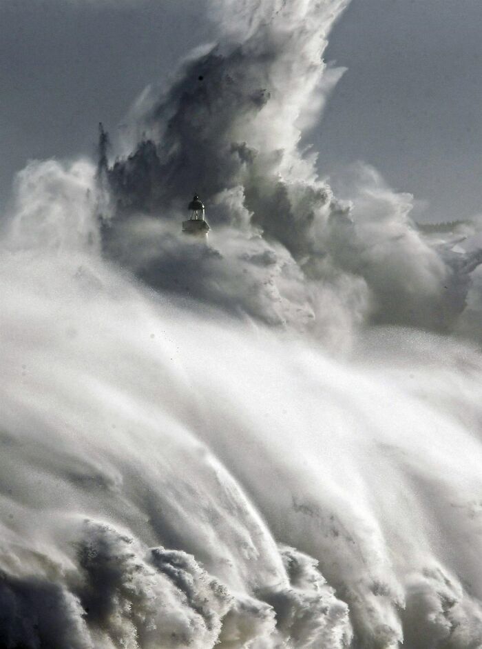 Massive ocean wave crashing over a lighthouse, highlighting the ocean's power and danger.