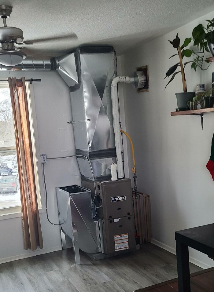 Oddly placed furnace and ductwork in a small apartment living room, showcasing a landlord's unusual installation decision.