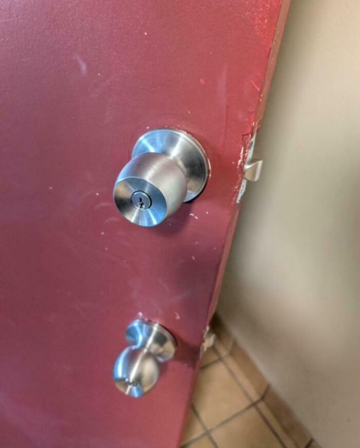 Red door with mismatched doorknobs, highlighting landlord issues.