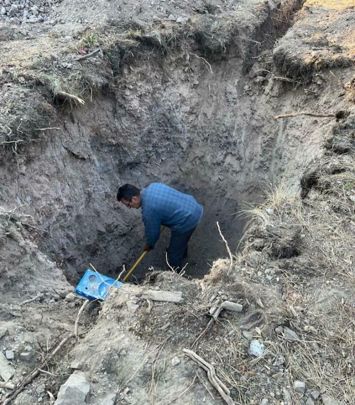 Man deep in a dug-out pit holding a shovel, illustrating a dangerous situation in a construction site.