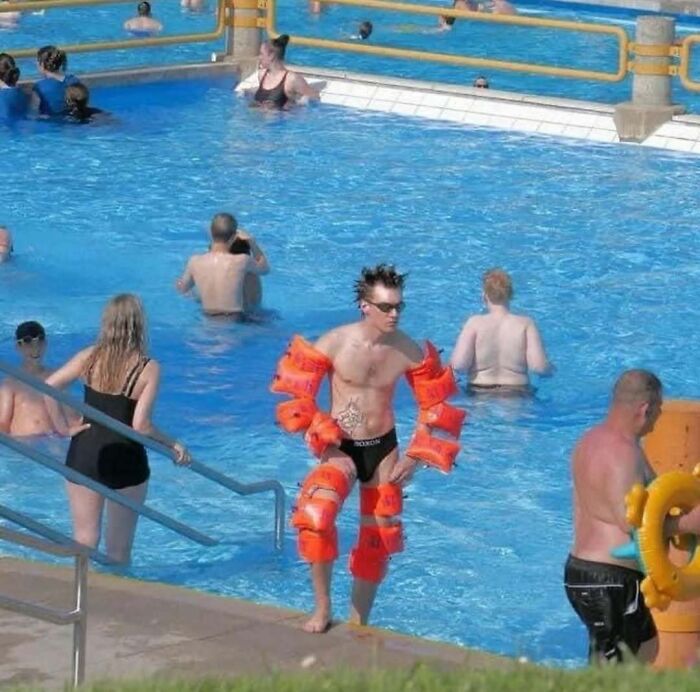 Man in pool covered with orange floaties; a humorous and random cursed image.