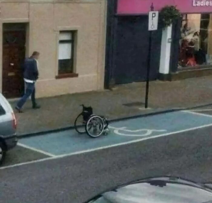 Wheelchair in a parking spot on the street, with a person walking by, illustrating a random cursed scenario.