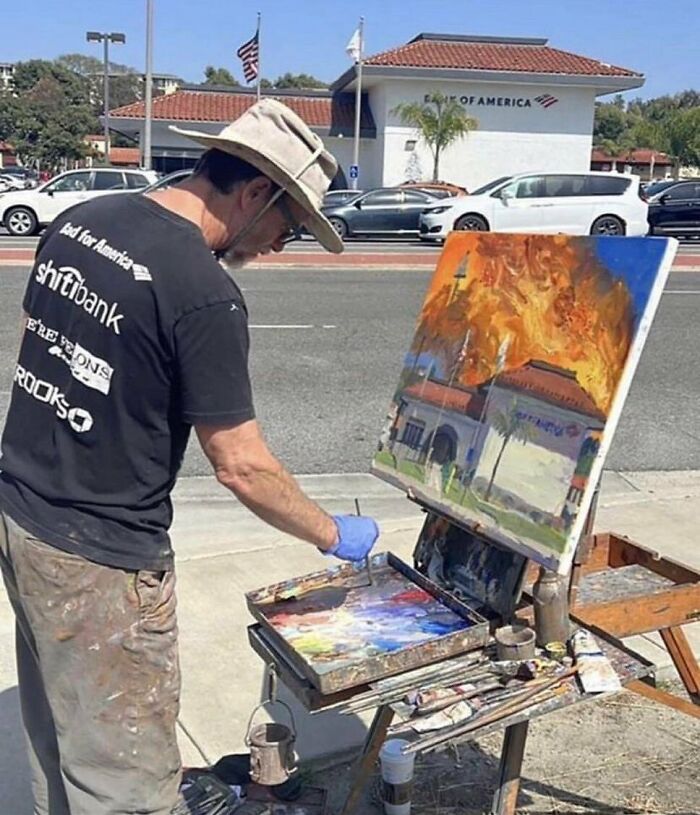 Painter creating artwork of a bank on fire, standing by an easel on a city sidewalk. Cursed images theme.