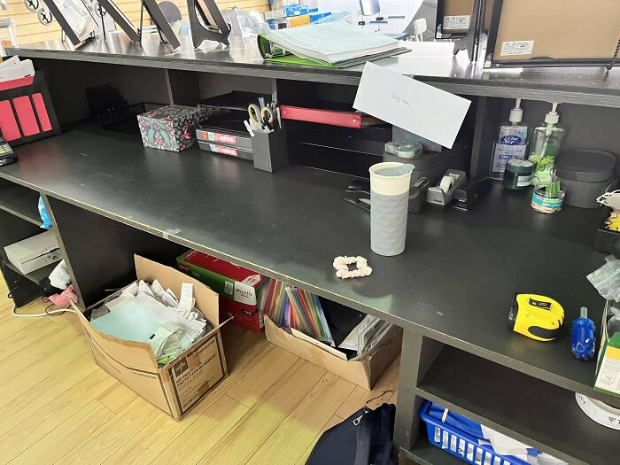 Office desk cluttered with supplies, folders, and a takeaway cup, reflecting frustrating bosses' disorganized workspaces.