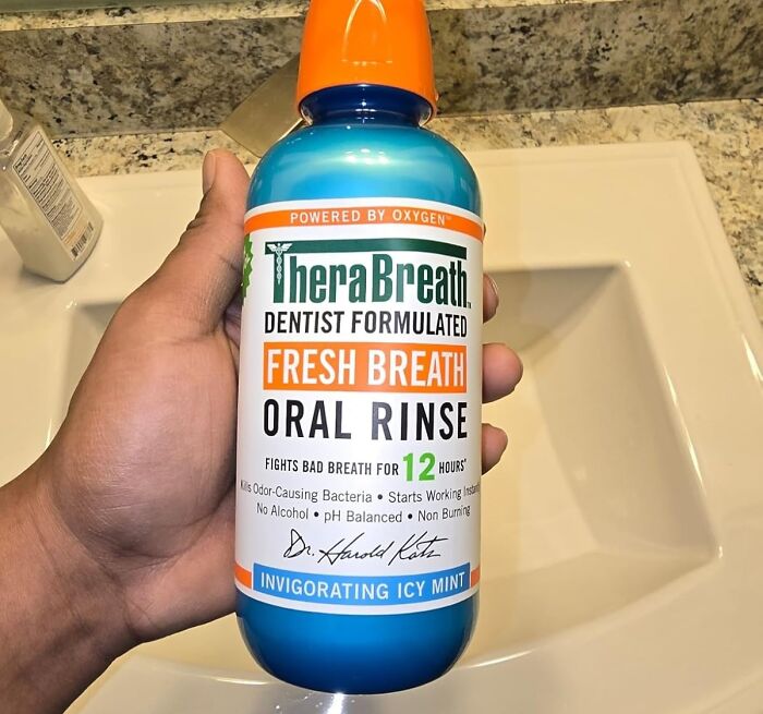 Hand holding TheraBreath Fresh Breath oral rinse by sink, dentist-formulated for 12-hour freshness. Featured in 40K review.
