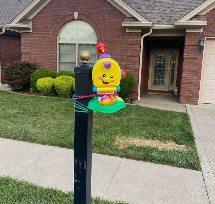 Toy repurposed as mailbox repair, attached with rope, in front of a house.