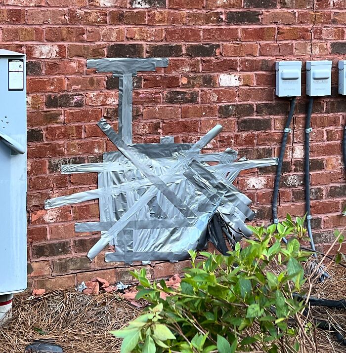 Failed repair attempt with duct tape on a brick wall, showing a messy patch job near utility meters.