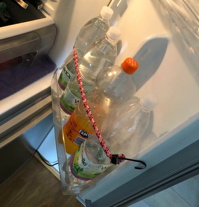 Refrigerator door bottles secured with a bungee cord in a repair attempt.