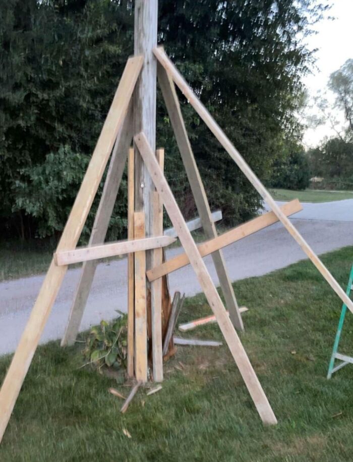 Failed repair attempt with mismatched wooden planks supporting a utility pole in grassy area.