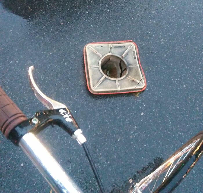 Failed repair attempt with removed drain cover on asphalt beside a bicycle handlebar.