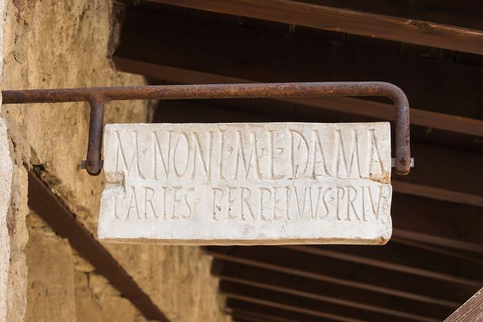 Ancient Roman Empire stone sign with Latin inscription, mounted on a rusted metal bracket.