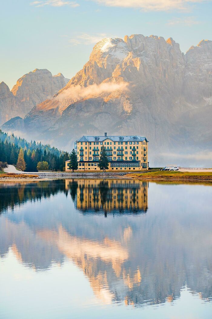 Majestic mountain landscape with a serene lake reflection and a charming building in the foreground.
