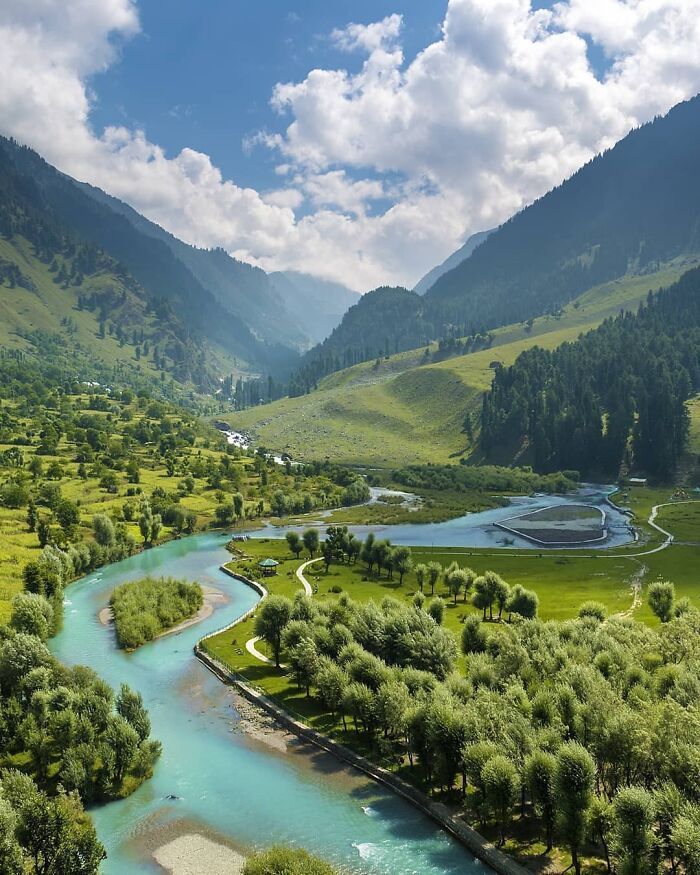 Scenic view of a beautiful place with a winding river, lush green valley, and mountainous backdrop under a cloudy sky.