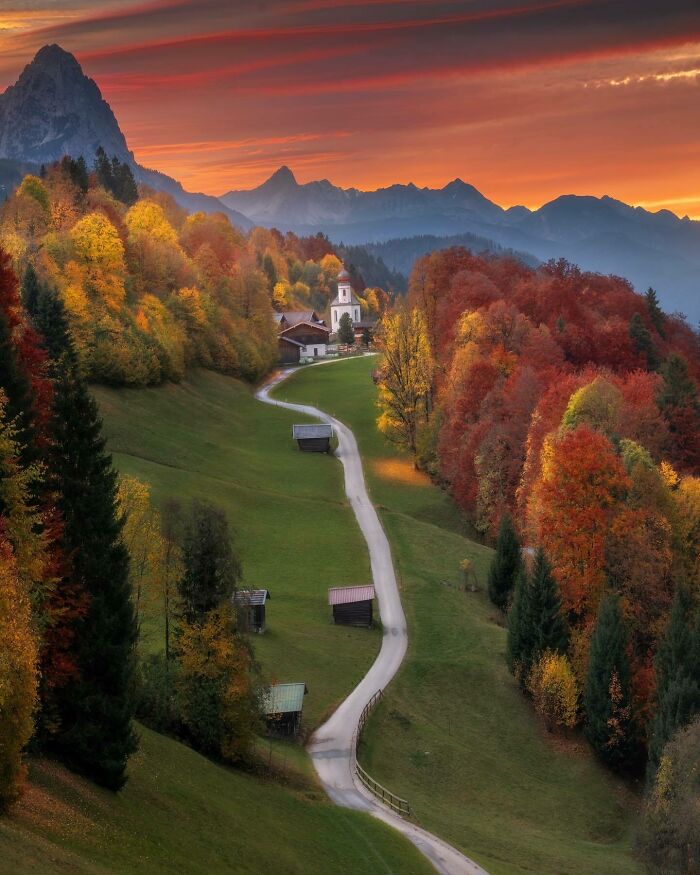 A winding path through vibrant autumn foliage leads to a church, showcasing a beautiful place in nature.