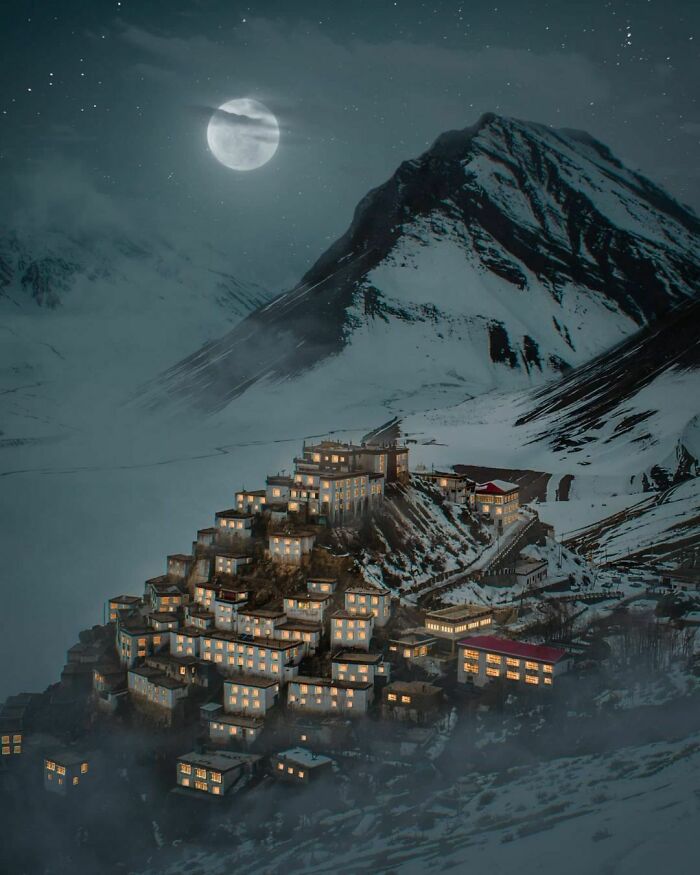 A village on a snowy mountain under a full moon, showcasing one of the most beautiful places discovered.