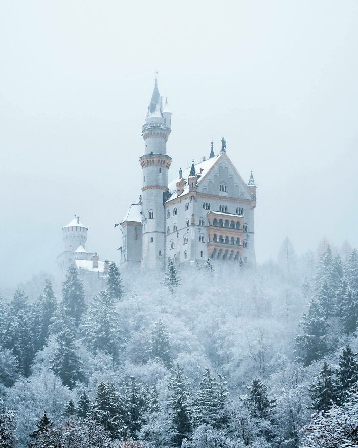 Majestic snowy castle rising above a wintry forest, showcasing one of the most beautiful places discovered.