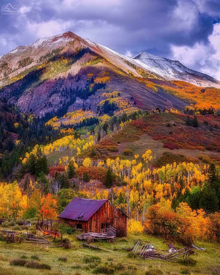 Rustic cabin in vibrant autumn foliage, set against majestic snow-capped mountains in a remote beautiful place.