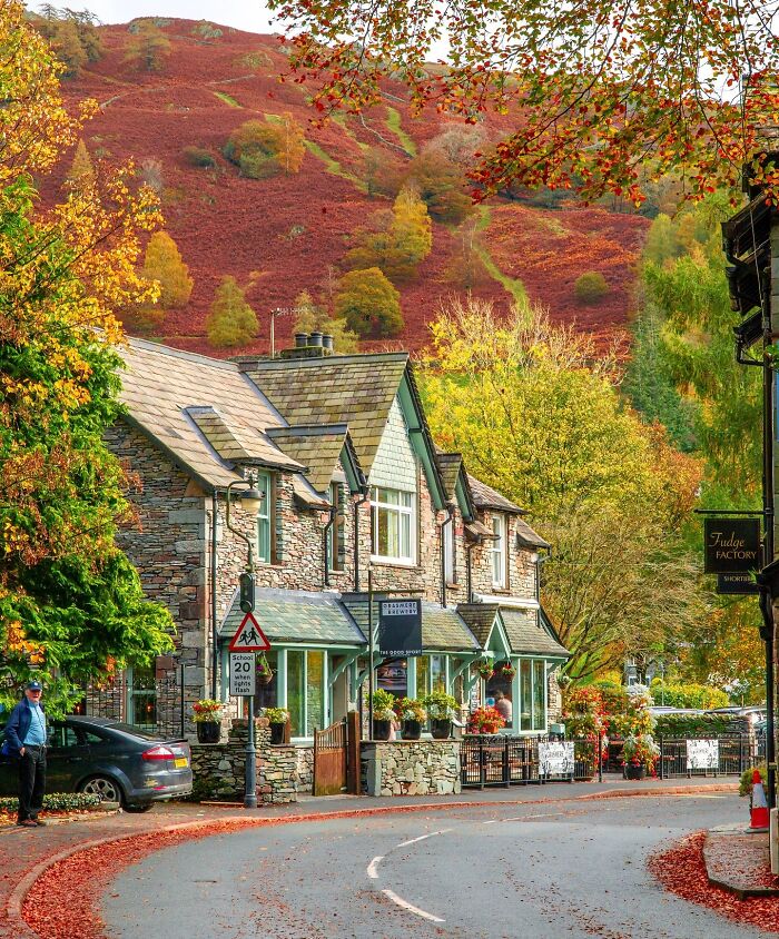Stone building with green trim surrounded by colorful autumn trees, set against a red hillside.