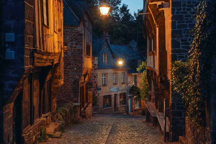 Narrow cobblestone street in a picturesque village, illuminated by warm streetlights.