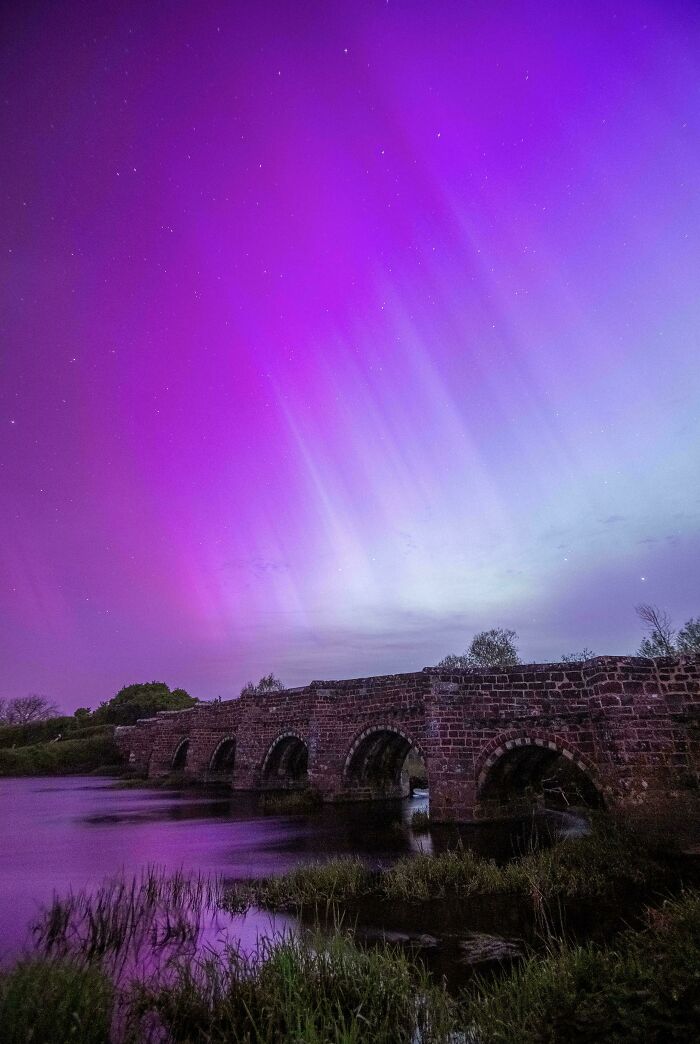 Ancient stone bridge under vivid purple aurora, showcasing a beautiful place.