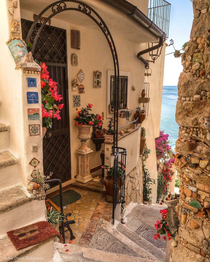 Charming coastal alley with vibrant flowers, ornate archway, and sea view, showcasing a beautiful place discovered.