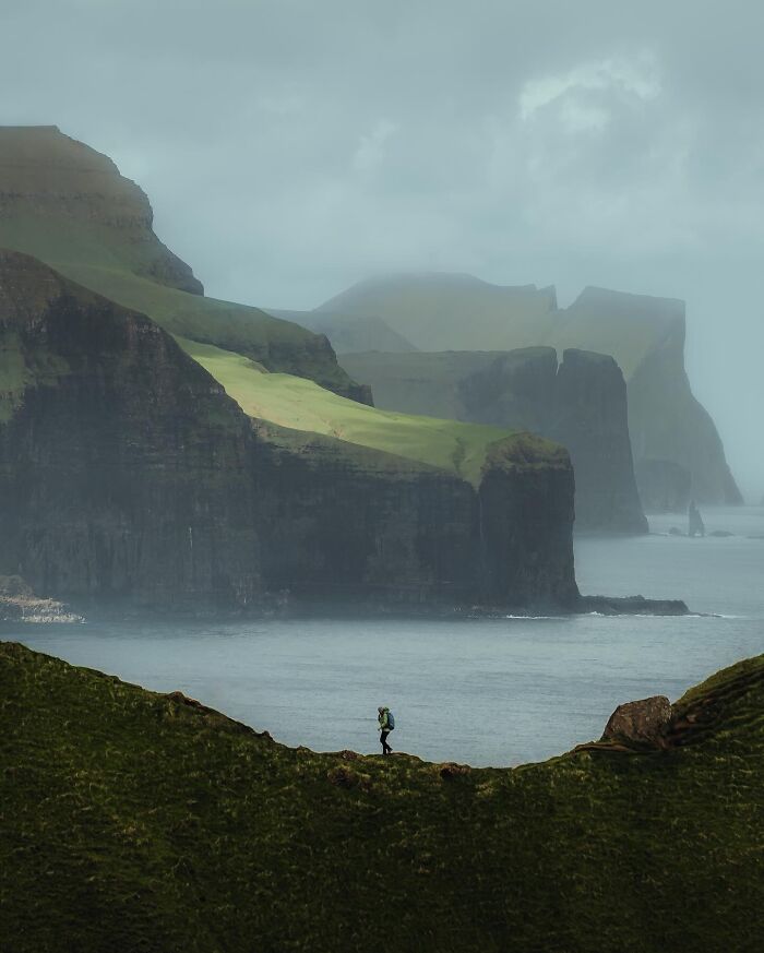 Hiker enjoying the breathtaking view of beautiful coastal cliffs in a misty landscape.