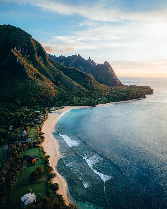 Aerial view of a beautiful beach with lush green cliffs and clear blue water at sunset.