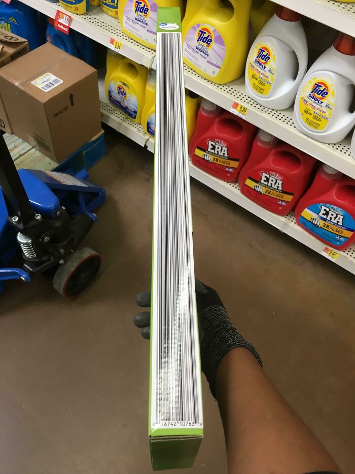 A gloved hand holding a thin book with a barcode, appearing surreal in a store aisle.